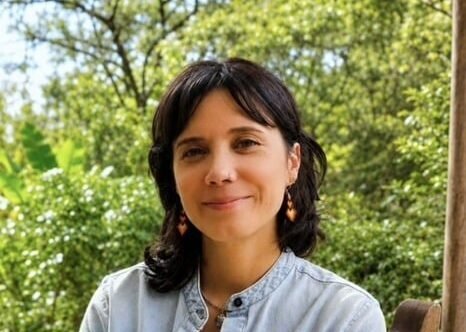 female therapist in blue shirt smiling with trees and bushes in the background