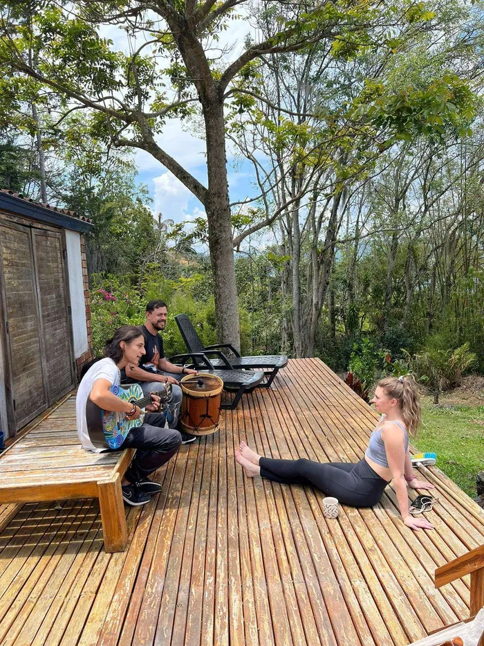 Harmonica Ayahuasca Retreat Colombia Morning on the deck Participants playing guitar and stretching on the wooden deck among tall trees